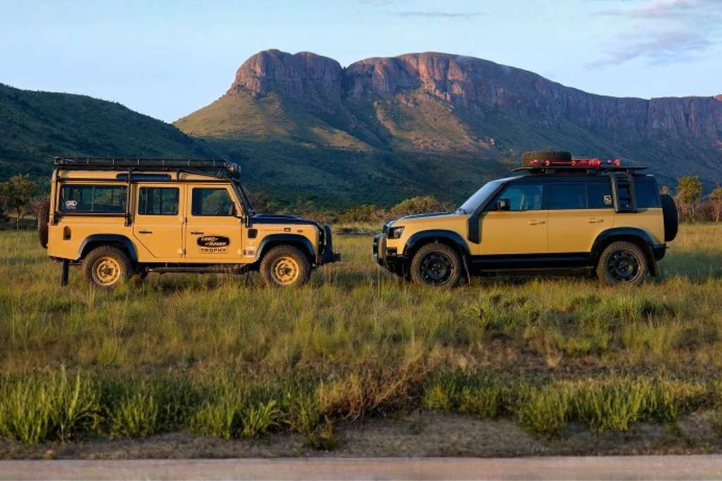 Dos camionetas Land Rover Defender amarillas estacionadas en un campo abierto con montañas al fondo durante el atardecer.